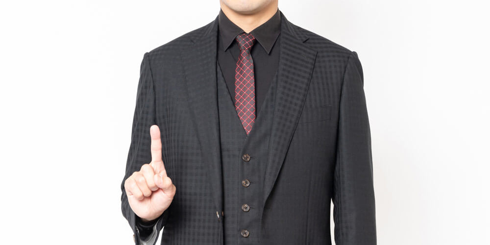 人差し指を立てるスーツ姿の男性